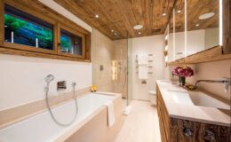 Modern bathroom design featuring a luxurious bathtub, walk-in shower, and elegant wooden accents. The space is illuminated with recessed lighting and has a stylish vanity with a double sink, creating a serene and inviting atmosphere.