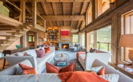 Spacious and cozy living room featuring wooden beams, large windows, and a modern fireplace, adorned with comfortable sofas and decorative pillows, creating a warm and inviting atmosphere.