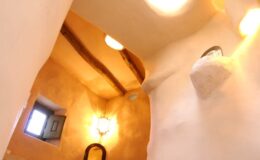 Interior view of a cozy, rustic hallway featuring warm earthen walls, wooden beams, and soft lighting, showcasing a small window and elegant wall sconces.