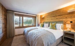 Cozy hotel bedroom featuring twin beds with plush bedding, wooden accent walls, and large windows showcasing a scenic view. Ideal for relaxation and comfort during a mountain getaway.