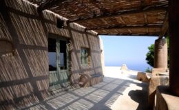 Cozy outdoor terrace with wooden beams casting shadows, overlooking a serene ocean view. Ideal for relaxation and enjoying nature.