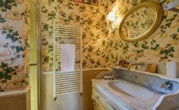 Vintage bathroom with floral wallpaper, marble sink, and towel rack, featuring a round mirror and warm lighting. Ideal for showcasing classic interior design.