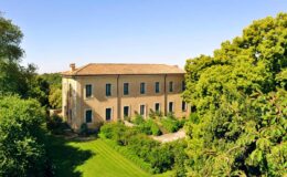 Historic countryside villa surrounded by lush greenery and trees under a clear blue sky. Ideal for nature retreats and scenic getaways.