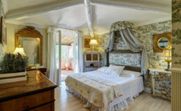 Cozy bedroom featuring a double bed with floral bedding, vintage decor, and soft lighting. The room has a rustic wooden dresser and a large window with a view, enhancing the inviting atmosphere.
