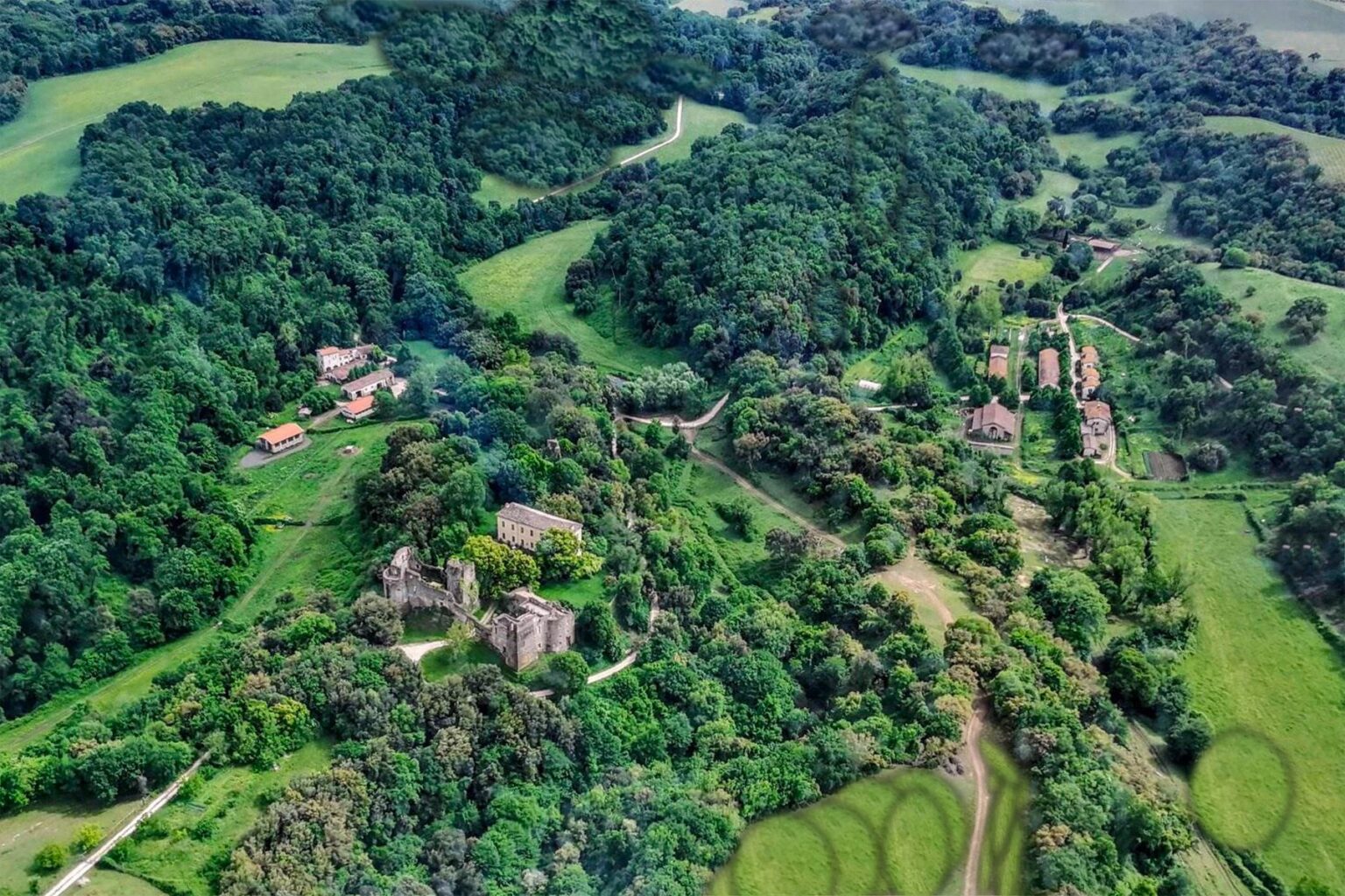Aerial view of a lush green landscape featuring a mix of forested areas and open fields, with scattered buildings nestled among the trees, showcasing the natural beauty of the countryside. | Only on SopranoVillas