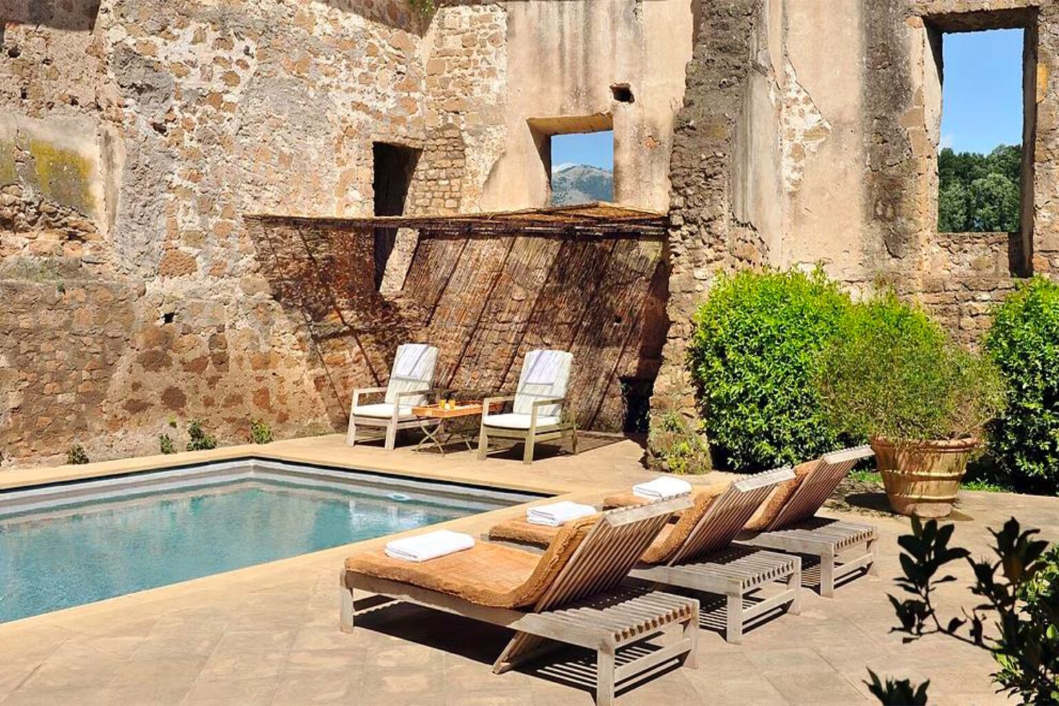 Rustic outdoor pool area with loungers surrounded by historical stone walls and lush greenery, creating a tranquil retreat. | Only on SopranoVillas