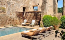 Rustic outdoor pool area with loungers surrounded by historical stone walls and lush greenery, creating a tranquil retreat.