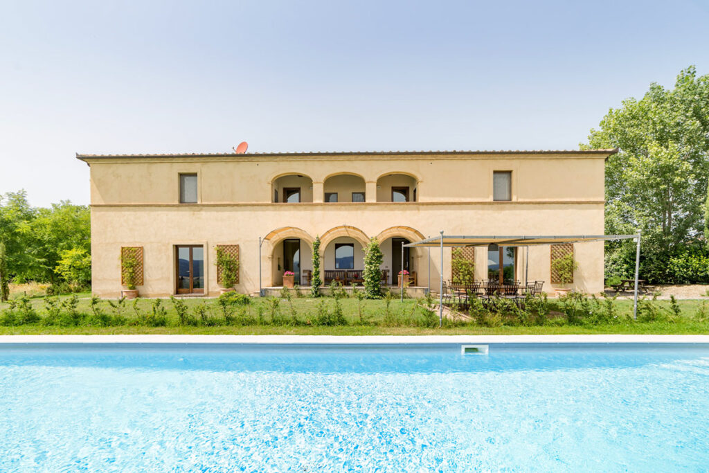 Elegant villa with arched windows and a spacious terrace, surrounded by greenery and featuring a serene swimming pool in the foreground. Ideal for luxury retreats and family vacations. | Only on SopranoVillas