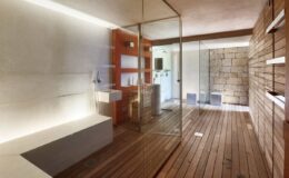 Modern bathroom interior design featuring wooden flooring, minimalist fixtures, and a spacious glass shower. The walls combine smooth surfaces with natural stone accents, creating a serene and stylish atmosphere. Soft lighting enhances the contemporary aesthetic.