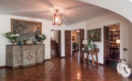 Spacious and elegantly designed foyer featuring a rustic wooden console table, decorative artwork, and potted plants, with a view of adjoining rooms and a staircase in a well-lit, inviting atmosphere.