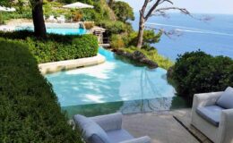 Scenic view of a luxurious infinity pool overlooking the ocean, surrounded by lush greenery and modern outdoor seating, ideal for relaxation and leisure.