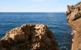 Rocky coastline overlooking calm blue ocean with clear sky. Ideal for nature photography and coastal scenery.