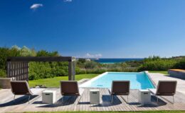 Luxury outdoor pool area with sun loungers and scenic ocean view under a clear blue sky. Ideal for relaxation and summer getaways.