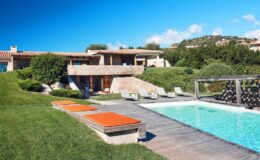Modern villa with a swimming pool and lounge chairs, surrounded by lush greenery and a clear blue sky. Ideal for luxury vacation rentals or outdoor gatherings.