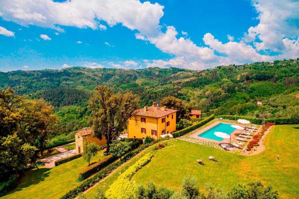 Scenic view of a countryside villa with a swimming pool, surrounded by lush green hills and blue skies, ideal for a relaxing getaway in nature. | Only on SopranoVillas