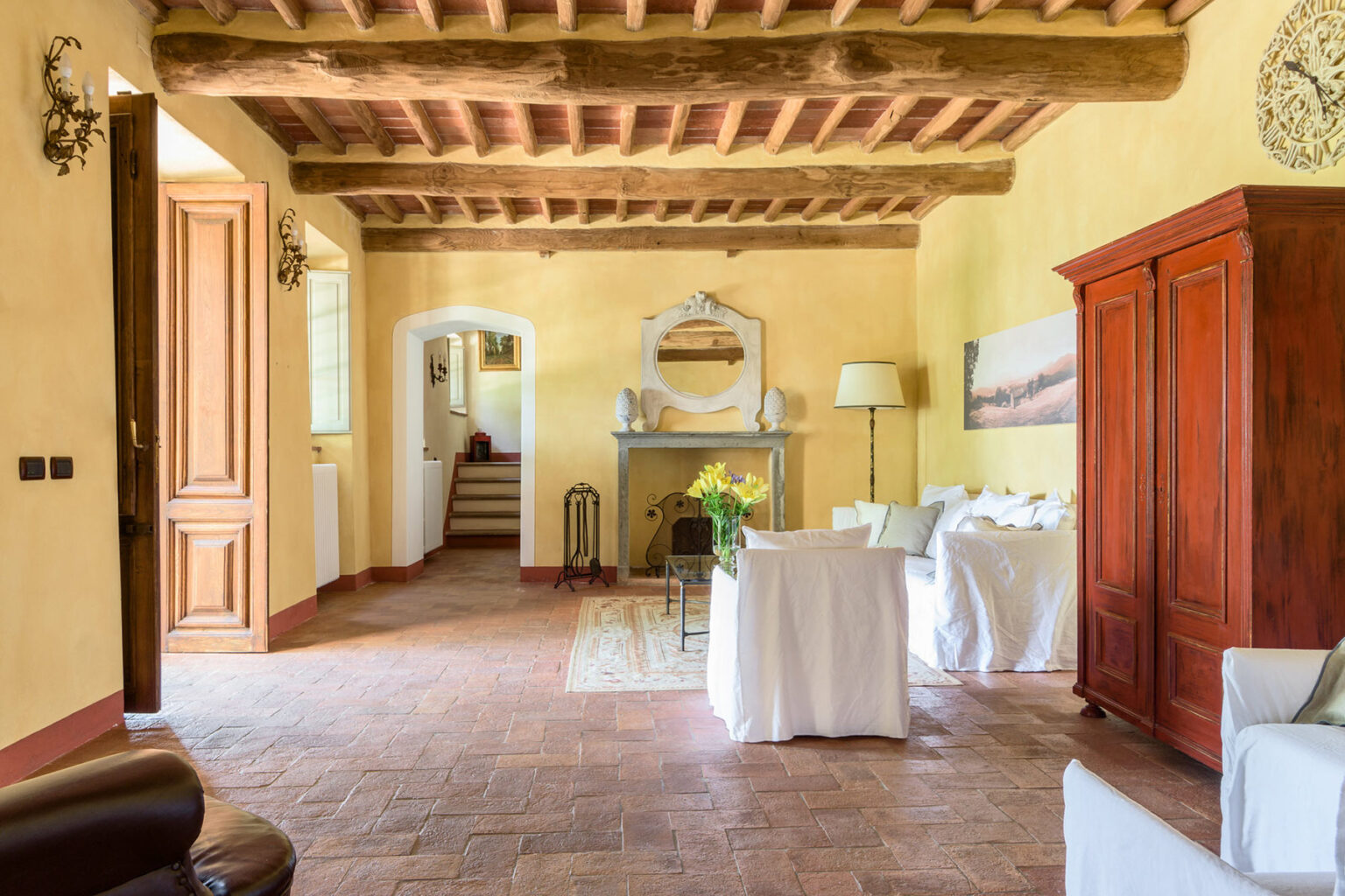 Spacious living room featuring rustic wooden beams, warm yellow walls, and terracotta flooring, with a cozy seating area and elegant wooden furniture. | Only on SopranoVillas