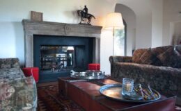 Cozy living room interior featuring a stone fireplace, plush sofas, and a wooden coffee table with decorative items, creating a warm and inviting atmosphere.