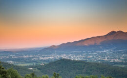 Scenic view of mountains at sunset, showcasing a vibrant sky with hues of orange and blue, overlooking a valley and a town below.
