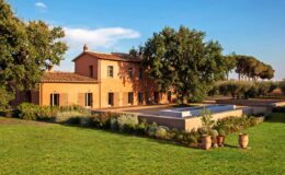 Rustic villa with a terracotta facade surrounded by lush greenery and a swimming pool, set against a clear blue sky. Ideal for a serene countryside retreat.