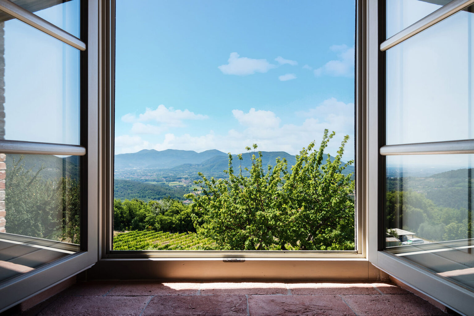 Scenic view from an open window showcasing a lush green landscape, rolling hills, and a clear blue sky with scattered clouds. Perfect for illustrating tranquility and nature. | Only on SopranoVillas