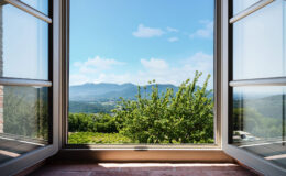 Scenic view from an open window showcasing a lush green landscape, rolling hills, and a clear blue sky with scattered clouds. Perfect for illustrating tranquility and nature.