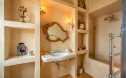 Elegant bathroom interior featuring a modern sink, decorative mirror, and stylish shelving. Soft lighting enhances the warm tones of the walls, creating a cozy atmosphere. Ideal for design inspiration and home decor ideas.