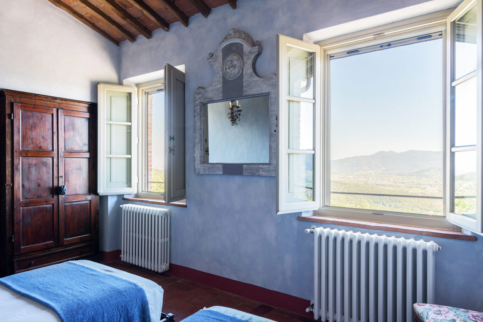 Spacious bedroom with mountain views, featuring open windows, a rustic wooden wardrobe, and a decorative mirror on the wall. The room showcases natural light and a cozy atmosphere, ideal for relaxation. | Only on SopranoVillas