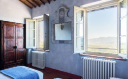 Spacious bedroom with mountain views, featuring open windows, a rustic wooden wardrobe, and a decorative mirror on the wall. The room showcases natural light and a cozy atmosphere, ideal for relaxation.