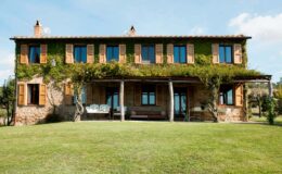 Charming rustic house with wooden shutters and a lush garden, featuring a covered porch and greenery, set against a clear blue sky. Ideal for showcasing countryside architecture and outdoor living.