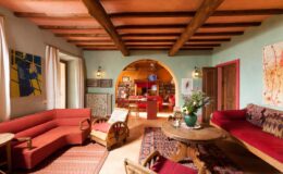Cozy living room featuring rustic wooden beams, red sofas, a wooden coffee table, and decorative art on the walls, creating an inviting and warm atmosphere.