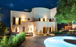 Modern villa at night with illuminated architecture, surrounded by lush greenery and a swimming pool, showcasing a contemporary design and inviting outdoor space.
