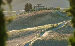 Scenic view of a hillside villa surrounded by rolling green fields and trees, bathed in warm sunlight during golden hour.