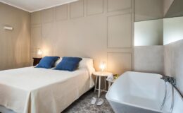 Cozy modern bedroom featuring a queen-sized bed with blue accent pillows, a stylish freestanding bathtub, and soft lighting, ideal for relaxation and comfort.