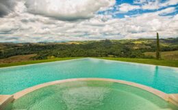Infinity pool overlooking lush green hills and a dramatic sky with clouds. Ideal for luxury retreats and vacation rentals.