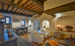 Cozy living room with rustic wooden beams, featuring a comfortable seating area, dining table, and warm decorative elements, creating an inviting atmosphere.