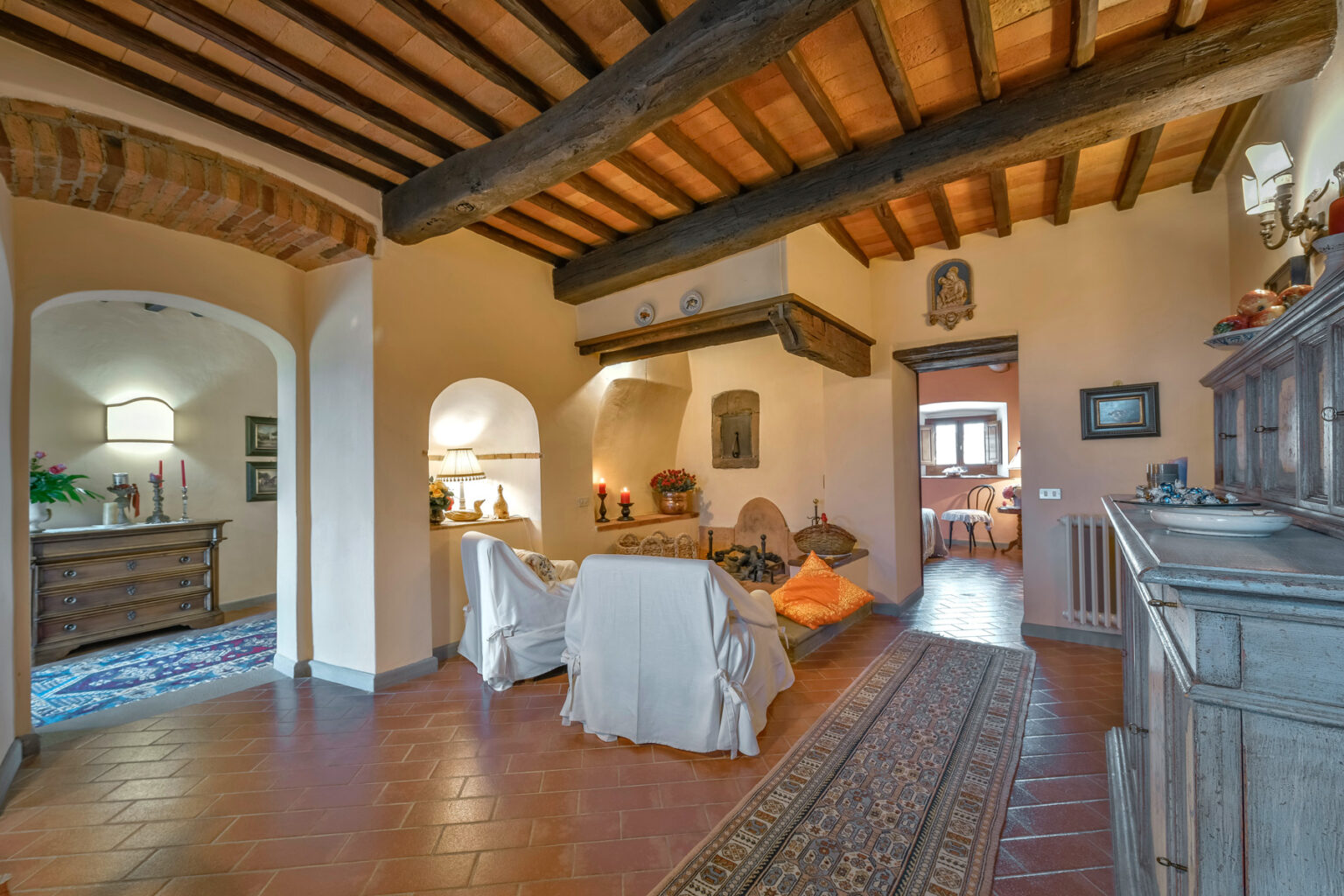 Cozy living room interior featuring rustic wooden beams, terracotta flooring, and warm lighting. The space includes comfortable seating, decorative art, and an inviting atmosphere, ideal for relaxation. | Only on SopranoVillas