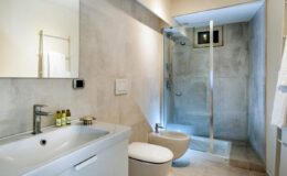 Modern bathroom interior featuring a sleek design with a shower, minimalist vanity, and neutral color palette. The space includes a wall-mounted mirror, contemporary fixtures, and stylish toiletries.