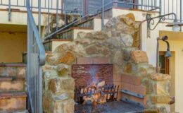 Stone outdoor fireplace with a metal grate, surrounded by stairs and a balcony, providing a cozy atmosphere for gatherings.
