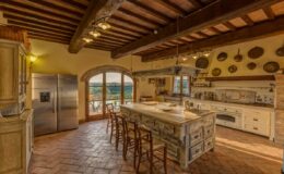Spacious rustic kitchen with wooden beams, a large central island, and modern appliances, featuring a scenic view through arched windows.