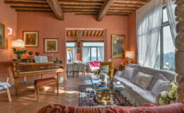 Cozy living room featuring wooden beams, warm peach walls, a grand piano, elegant furniture, and natural light streaming through large windows, creating an inviting atmosphere.