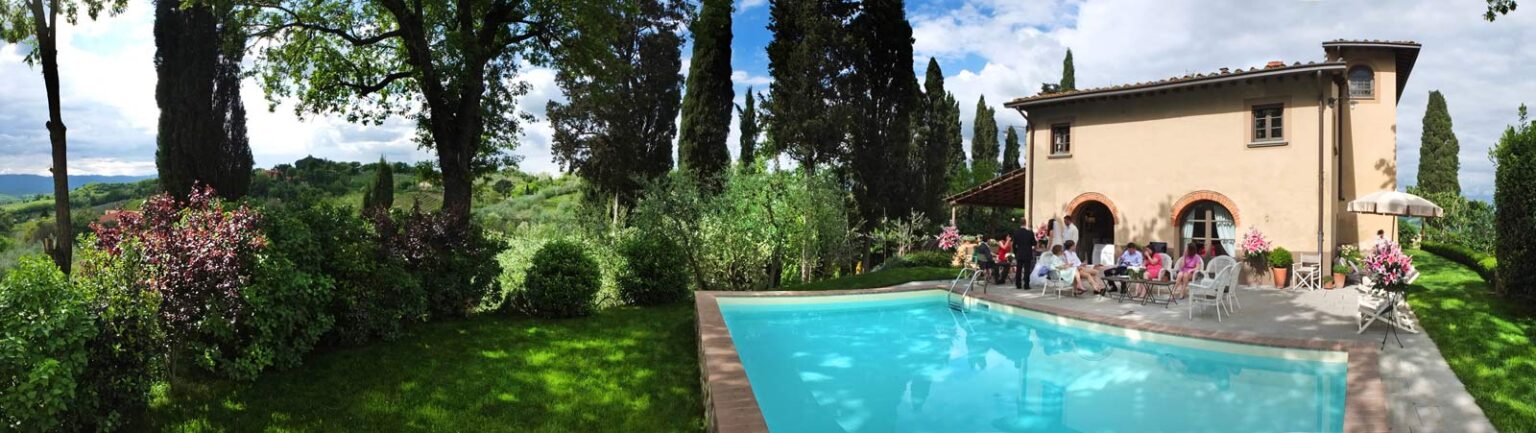 Beautiful outdoor pool surrounded by lush greenery and tall cypress trees, with a charming villa in the background. People are enjoying a sunny day by the pool, creating a relaxing atmosphere in a picturesque setting. Perfect for vacation or leisure activities. | Only on SopranoVillas