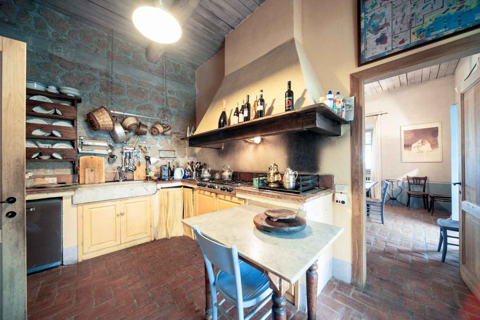 Spacious kitchen with wooden cabinets, a marble table, and rustic decor, featuring a stove, cookware, and artistic wall hangings, creating a warm and inviting atmosphere. | Only on SopranoVillas