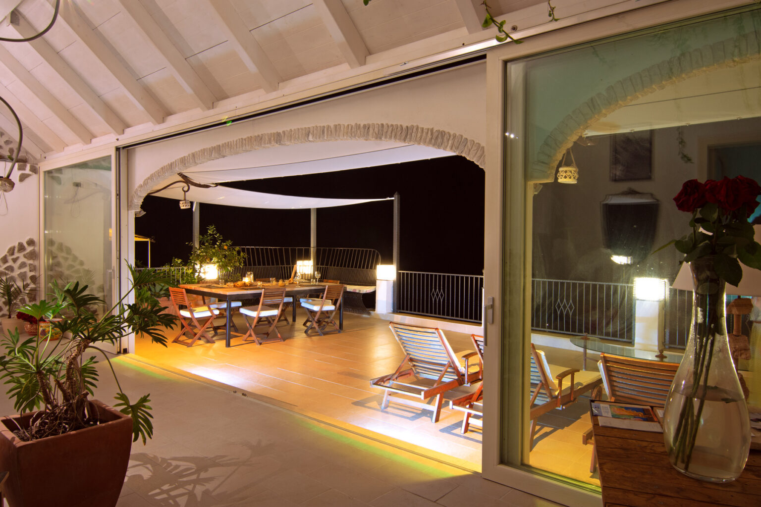 Spacious outdoor terrace with dining table and lounge chairs, illuminated at night, showcasing a cozy and inviting atmosphere. | Only on SopranoVillas