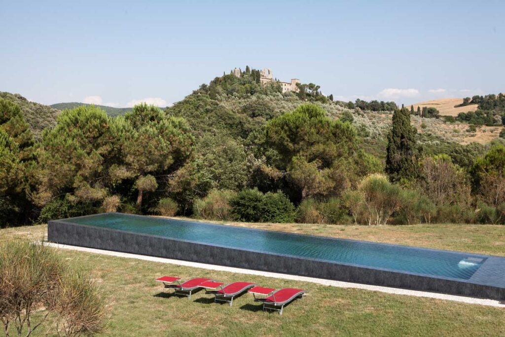 Modern infinity pool overlooking lush greenery and rolling hills, with red lounge chairs arranged on the side, ideal for outdoor relaxation and serene views. | Only on SopranoVillas