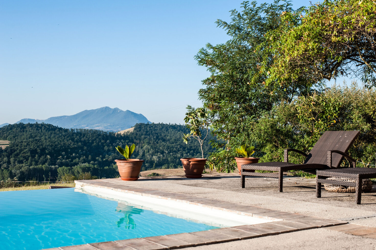Scenic outdoor poolside view with lounge chairs, surrounded by lush greenery and mountains in the background, ideal for relaxation and leisure. | Only on SopranoVillas