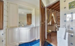 Bright and spacious bathroom featuring white cabinetry, blue tiled flooring, and elegant decor, including curtains and a towel rack, creating a cozy and inviting atmosphere.