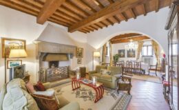 Cozy living room with wooden beams, a stone fireplace, and elegant furnishings, featuring a comfortable seating area, decorative artwork, and a dining space in a stylish interior.