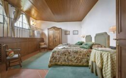 Cozy bedroom interior featuring a wooden ceiling, patterned bedding, vintage furniture, and soft green accents, creating a warm and inviting atmosphere.