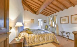 Cozy bedroom with wooden beams, featuring two twin beds with decorative bedding, a bedside lamp, and artwork on the walls, creating a warm and inviting atmosphere.