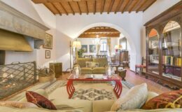 Spacious living room featuring wooden beams, a cozy fireplace, elegant furniture, and a large bookshelf, creating a warm and inviting atmosphere.